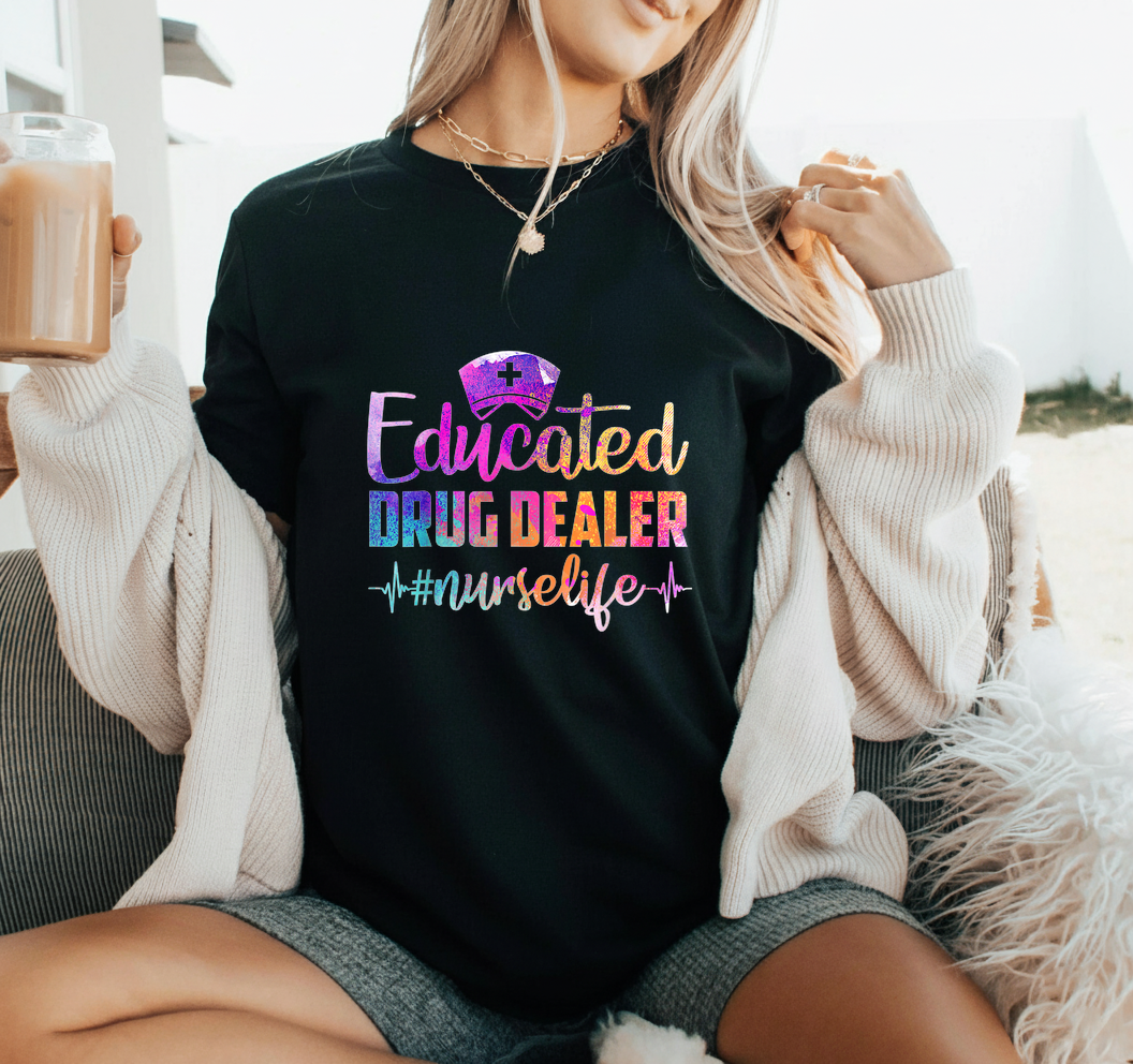Person wearing a black t-shirt with colorful text 'Educated Drug Dealer #nurselife' while holding a drink.