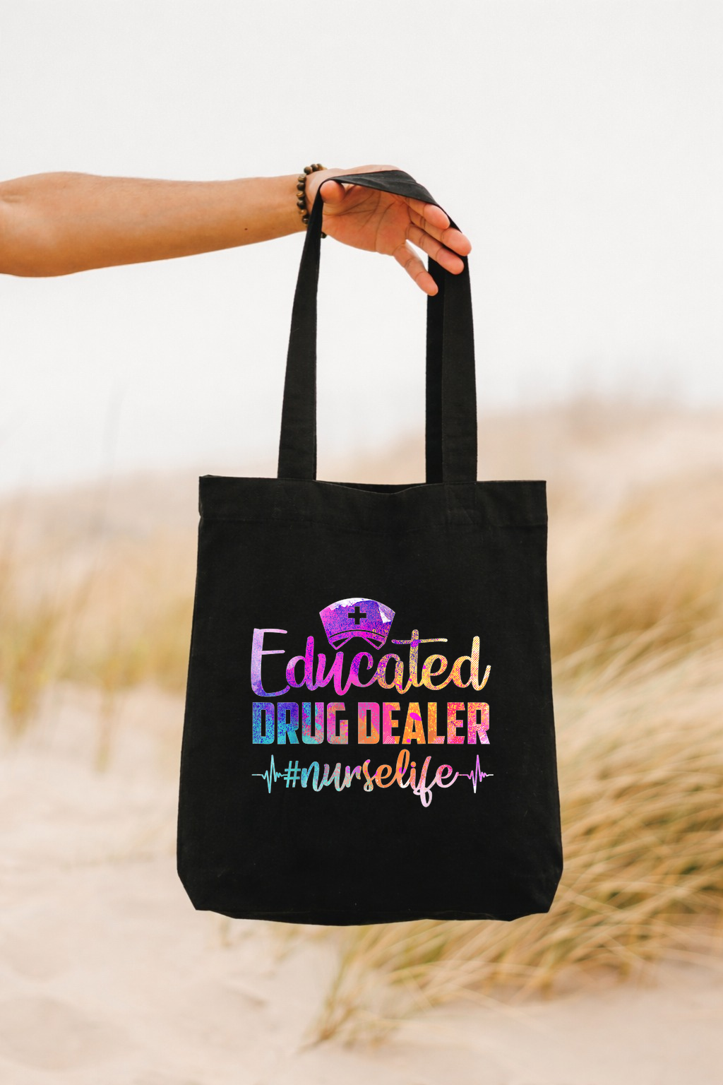 Black tote bag with colorful text held by a person against a blurred natural background